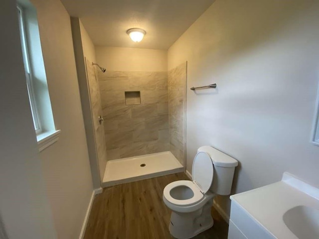 bathroom with tiled shower, wood-type flooring, vanity, and toilet