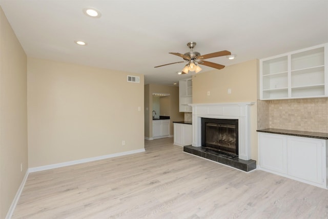 unfurnished living room with a tiled fireplace, ceiling fan, and light hardwood / wood-style floors