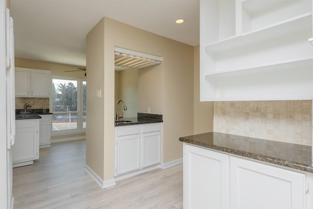 kitchen featuring decorative backsplash, white cabinets, dark stone counters, and light wood-type flooring