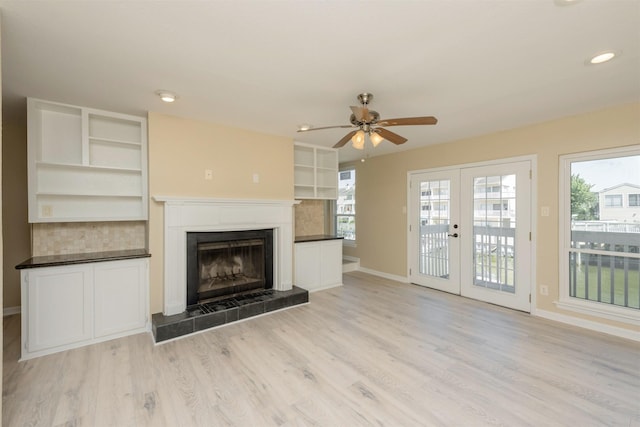 unfurnished living room with ceiling fan, a tiled fireplace, light hardwood / wood-style flooring, and french doors