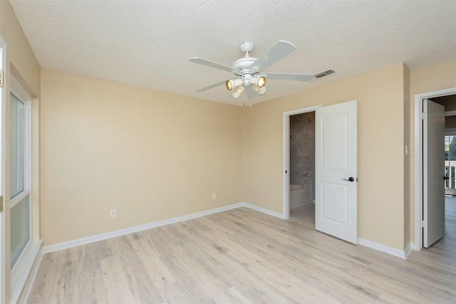 unfurnished bedroom featuring a textured ceiling, light hardwood / wood-style floors, ensuite bath, and ceiling fan