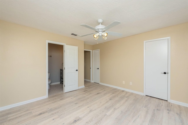 unfurnished bedroom with ceiling fan, ensuite bathroom, a textured ceiling, and light wood-type flooring