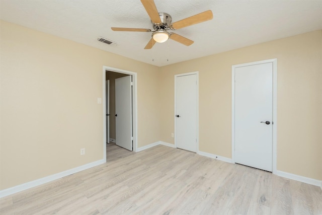 unfurnished bedroom featuring ceiling fan, light wood-type flooring, a textured ceiling, and two closets