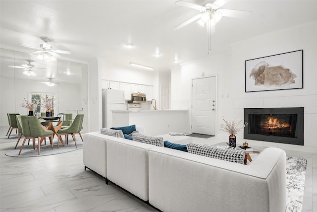 living room featuring a tile fireplace, ceiling fan, ornamental molding, and sink