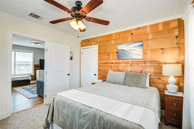 bedroom with hardwood / wood-style floors, wooden walls, ceiling fan, and ornamental molding