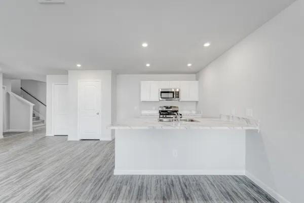 kitchen with white cabinets, hardwood / wood-style flooring, kitchen peninsula, and appliances with stainless steel finishes