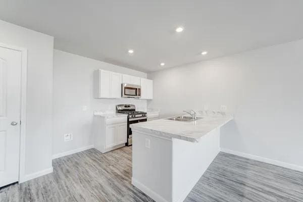 kitchen featuring white cabinets, sink, light hardwood / wood-style flooring, kitchen peninsula, and stainless steel appliances