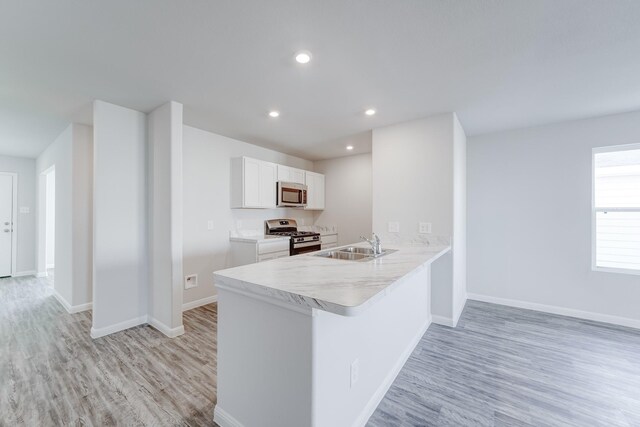 kitchen with sink, stainless steel appliances, kitchen peninsula, white cabinets, and light wood-type flooring