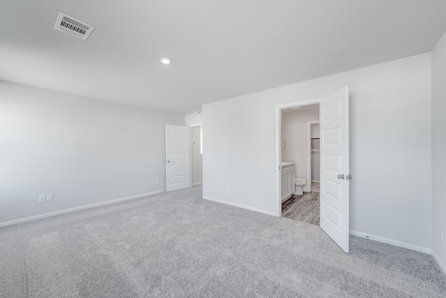 unfurnished bedroom featuring light carpet and connected bathroom