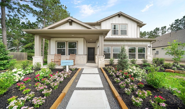 view of front of property with stone siding, fence, covered porch, and board and batten siding