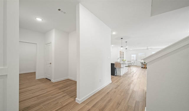 hall featuring baseboards, light wood-style flooring, visible vents, and recessed lighting