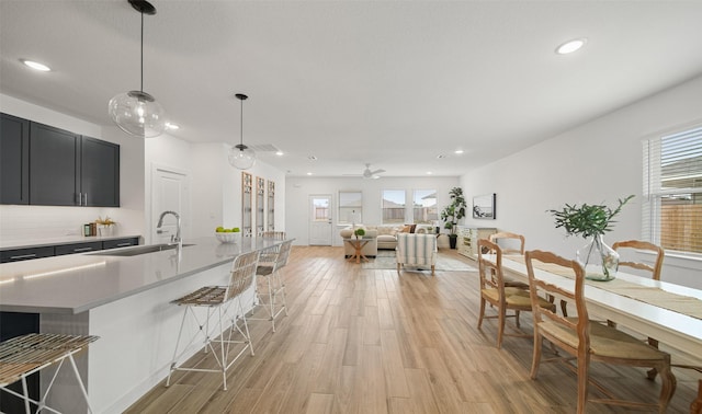 kitchen with a breakfast bar, pendant lighting, light countertops, a sink, and light wood-type flooring