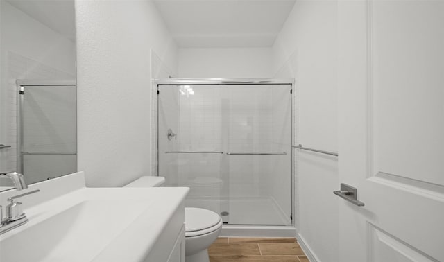 full bath featuring toilet, a stall shower, vanity, and wood finish floors