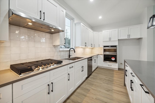 kitchen featuring sink, light wood-type flooring, appliances with stainless steel finishes, tasteful backsplash, and white cabinetry