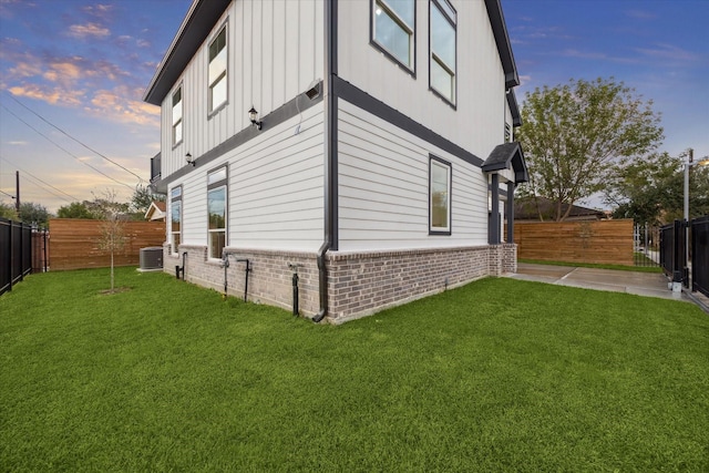 property exterior at dusk featuring a lawn and central AC