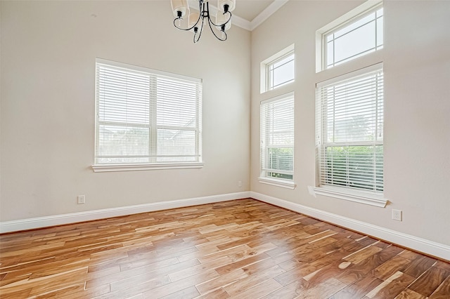 spare room with crown molding, a healthy amount of sunlight, a notable chandelier, and light wood-type flooring