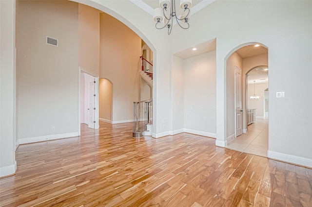 empty room featuring a notable chandelier, a high ceiling, and light hardwood / wood-style flooring