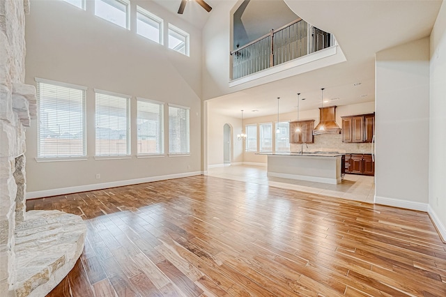 unfurnished living room with a stone fireplace, ceiling fan, light hardwood / wood-style floors, and a high ceiling