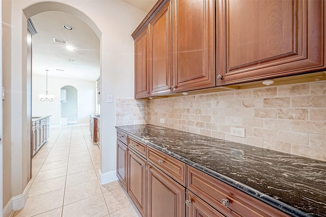 kitchen featuring tasteful backsplash, dark stone countertops, light tile patterned floors, and hanging light fixtures