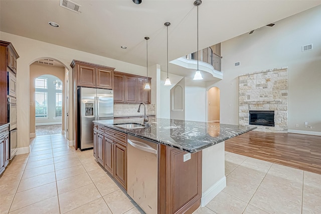 kitchen with sink, pendant lighting, dark stone counters, a center island with sink, and appliances with stainless steel finishes