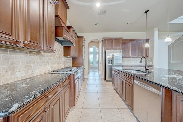 kitchen with tasteful backsplash, stainless steel appliances, sink, pendant lighting, and dark stone countertops