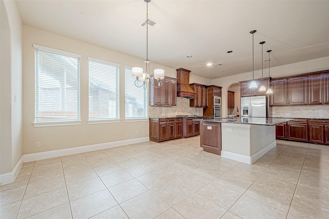 kitchen featuring premium range hood, backsplash, decorative light fixtures, a kitchen island with sink, and appliances with stainless steel finishes