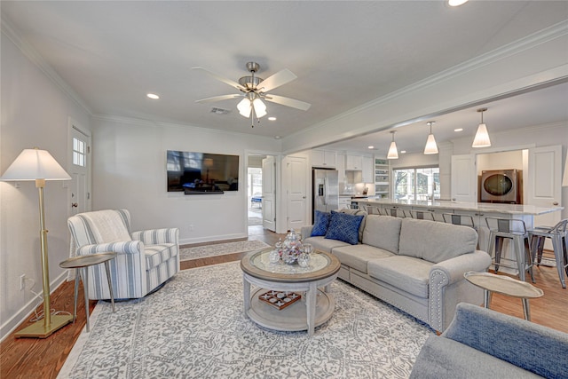 living room featuring stacked washer and clothes dryer, light hardwood / wood-style floors, ceiling fan, and ornamental molding