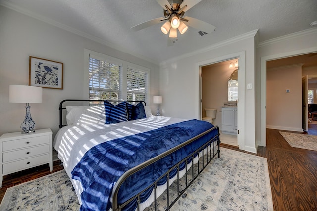 bedroom with wood finished floors, ornamental molding, a textured ceiling, baseboards, and connected bathroom