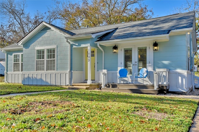 single story home featuring a front yard, french doors, and a shingled roof
