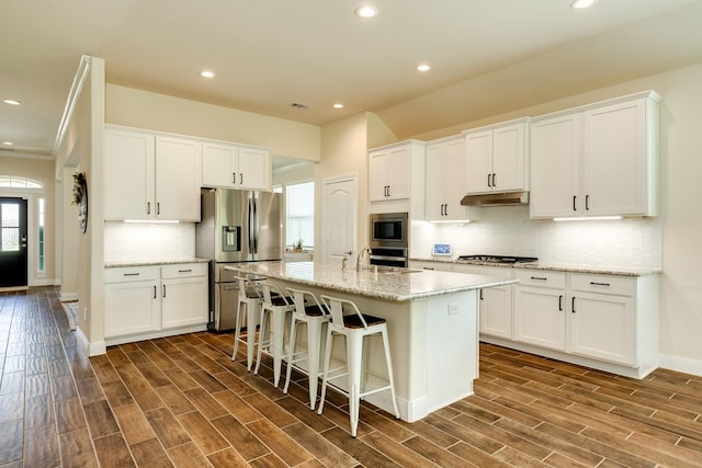 kitchen with appliances with stainless steel finishes, a center island with sink, white cabinetry, and dark wood-type flooring