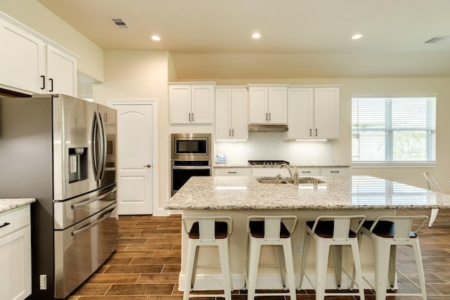 kitchen with a center island with sink, sink, light stone countertops, appliances with stainless steel finishes, and dark hardwood / wood-style flooring