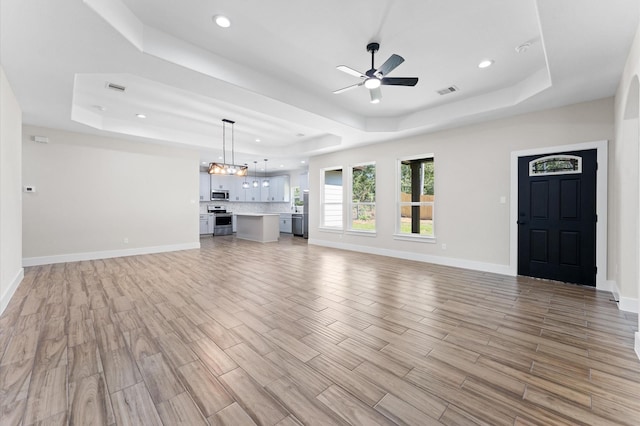 unfurnished living room featuring a raised ceiling, light hardwood / wood-style floors, and ceiling fan with notable chandelier