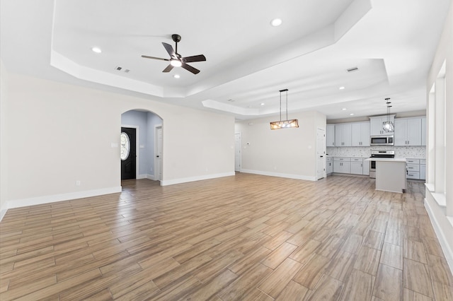 unfurnished living room with a tray ceiling, ceiling fan, and light hardwood / wood-style floors