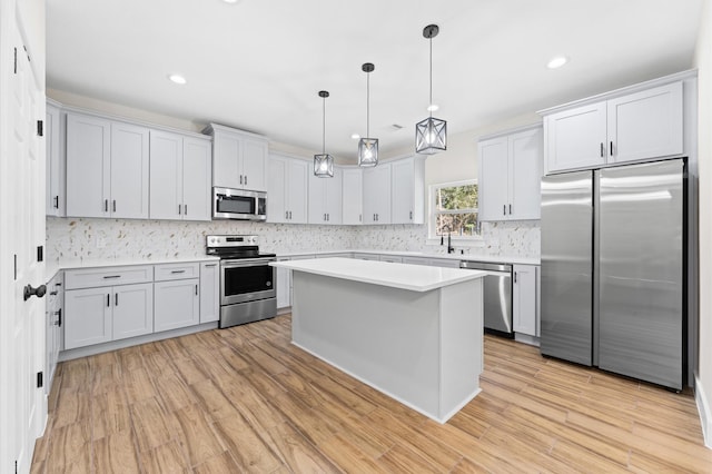 kitchen with decorative light fixtures, a center island, appliances with stainless steel finishes, and light hardwood / wood-style flooring