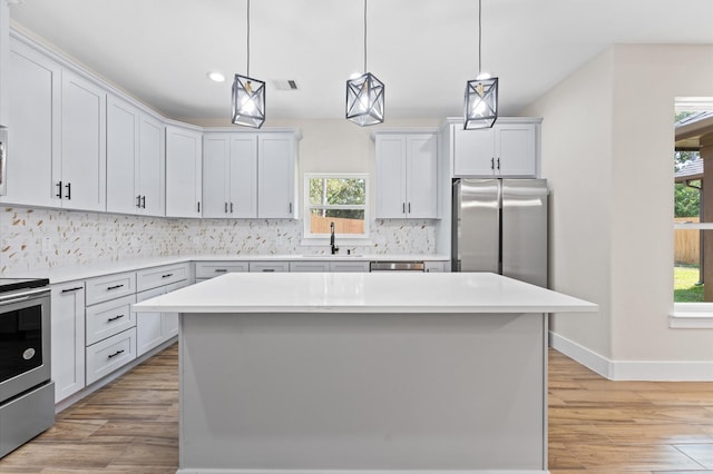 kitchen featuring appliances with stainless steel finishes, light hardwood / wood-style flooring, a kitchen island, and pendant lighting