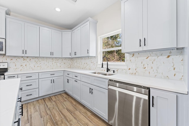 kitchen with sink, tasteful backsplash, stainless steel dishwasher, light hardwood / wood-style floors, and white cabinets