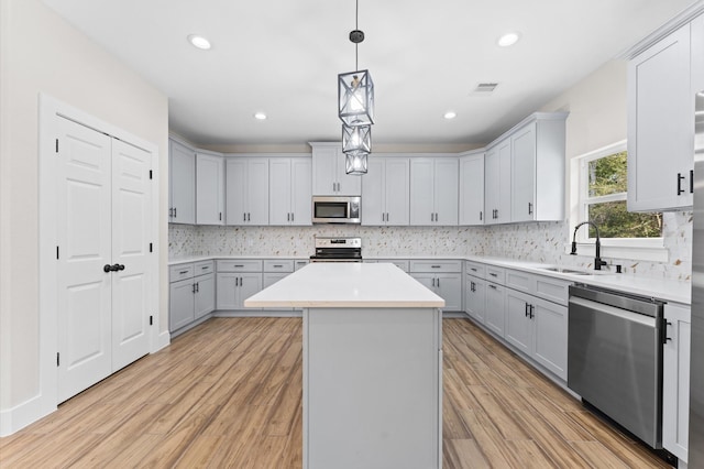 kitchen with sink, a center island, stainless steel appliances, light hardwood / wood-style flooring, and decorative light fixtures