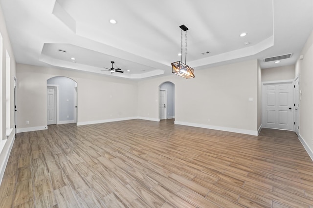 unfurnished living room with ceiling fan, light hardwood / wood-style floors, and a raised ceiling