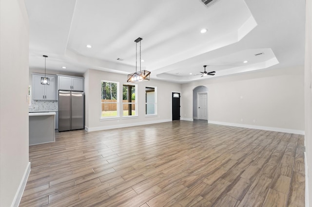 unfurnished living room featuring ceiling fan, light hardwood / wood-style flooring, and a tray ceiling