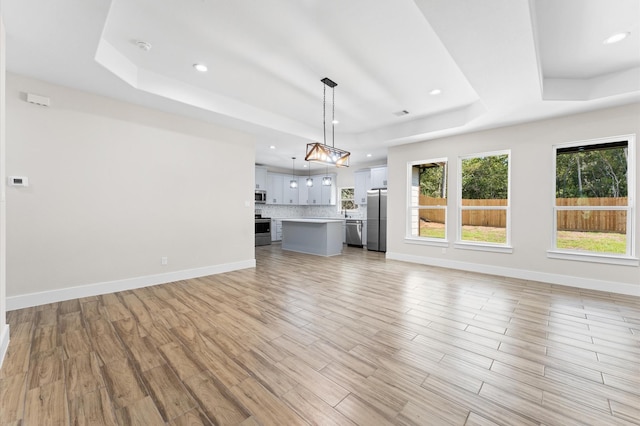 unfurnished living room featuring a tray ceiling and light hardwood / wood-style floors