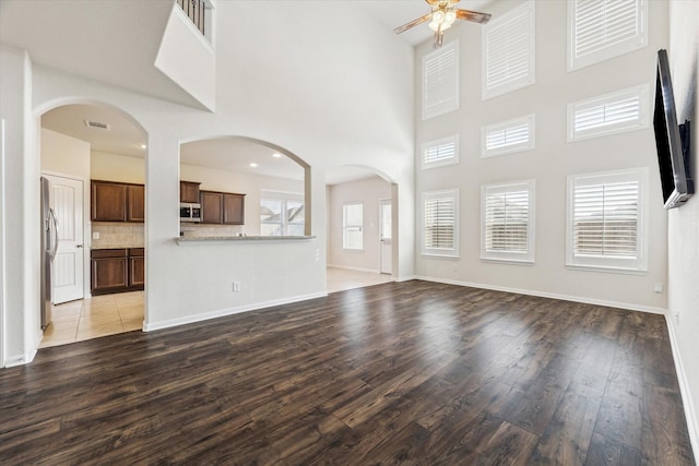 unfurnished living room with wood-type flooring, plenty of natural light, a high ceiling, and ceiling fan