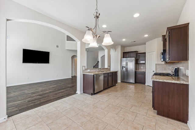 kitchen with light stone counters, a chandelier, pendant lighting, dark brown cabinets, and appliances with stainless steel finishes