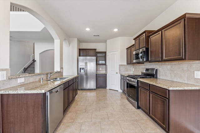 kitchen with dark brown cabinets, stainless steel appliances, light stone counters, and sink