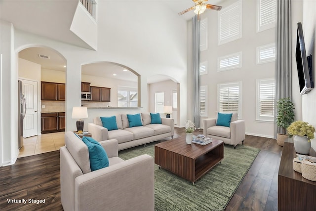 living room featuring a high ceiling, ceiling fan, a healthy amount of sunlight, and dark hardwood / wood-style floors