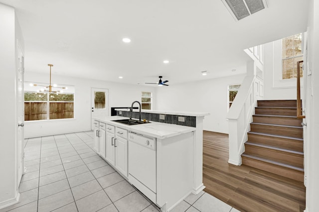 kitchen featuring white dishwasher, sink, a center island with sink, white cabinetry, and hanging light fixtures