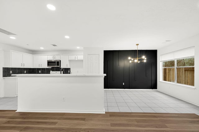 kitchen with white cabinets, backsplash, light wood-type flooring, and hanging light fixtures