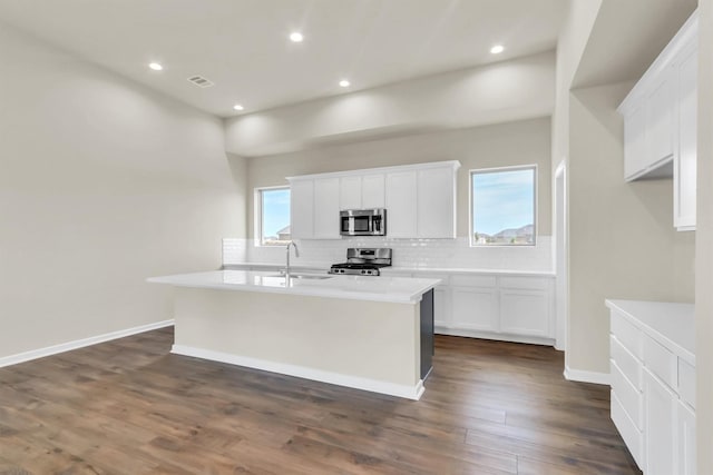 kitchen featuring white cabinets, decorative backsplash, an island with sink, dark hardwood / wood-style flooring, and stainless steel appliances