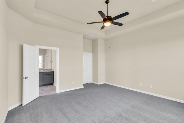 unfurnished room featuring a raised ceiling, ceiling fan, and light colored carpet