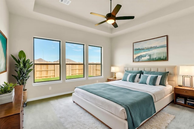 bedroom with ceiling fan, a raised ceiling, and light colored carpet