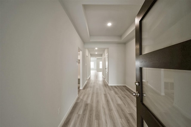 hall with light wood-type flooring and a raised ceiling